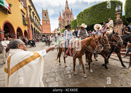 Mexikanischen Cowboys sind mit Weihwasser besprengt durch katholische Priester den Segen ihrer Wallfahrt während des Festivals von St. Michael in San Miguel de Allende, Mexiko. Stockfoto