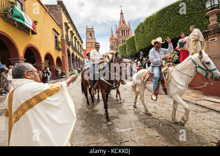 Mexikanischen Cowboys sind mit Weihwasser besprengt durch katholische Priester den Segen ihrer Wallfahrt während des Festivals von St. Michael in San Miguel de Allende, Mexiko. Stockfoto