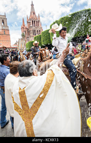 Mexikanischen Cowboys sind mit Weihwasser besprengt durch katholische Priester den Segen ihrer Wallfahrt während des Festivals von St. Michael in San Miguel de Allende, Mexiko. Stockfoto