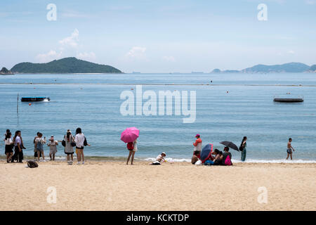 Strand mit Besuchern aus Tour Busse nehmen Fotogelegenheiten. Inseln einschließlich Tau Chau und nahen Insel im Hintergrund. Repulse Bay, Hong Kong Stockfoto