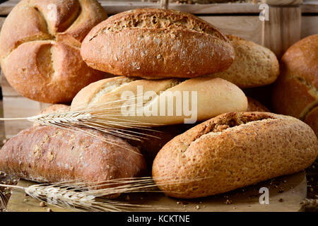 Nahaufnahme einer Auswahl an verschiedenen Brötchen und einige Ähren auf einem rustikalen Holztisch Stockfoto