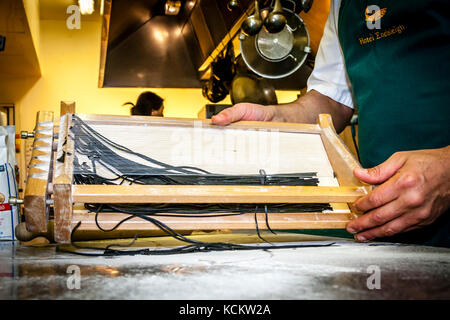 Die einzelnen Schritte der Pasta-Produktion mit dem Carraturo. Zuerst wird der Teig mehrmals durch eine Pasta-Maschine gedreht, bis er ziemlich dünn ist. Dann kann die dünne Teigklappe mit einem Nudelholz durch die Drähte gedrückt werden, die sie in dünne Streifen schneiden. Dann kurz Mehl und kochen in Salzwasser bis al dente kurz vor dem Essen. An der Seite des Küchenchefs steht Salvatore Piacente, ebenfalls Absolvent der Kochschule Santa Maria, wo José Graziosi bereits sein Handwerk gelernt hat Stockfoto