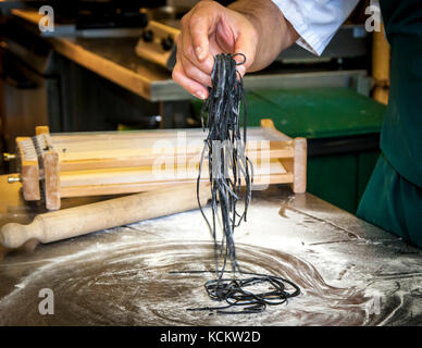 Die einzelnen Schritte der Pasta-Produktion mit dem Carraturo. Zuerst wird der Teig mehrmals durch eine Pasta-Maschine gedreht, bis er ziemlich dünn ist. Dann kann die dünne Teigklappe mit einem Nudelholz durch die Drähte gedrückt werden, die sie in dünne Streifen schneiden. Dann kurz Mehl und kochen in Salzwasser bis al dente kurz vor dem Essen. An der Seite des Küchenchefs steht Salvatore Piacente, ebenfalls Absolvent der Kochschule Santa Maria, wo José Graziosi bereits sein Handwerk gelernt hat Stockfoto