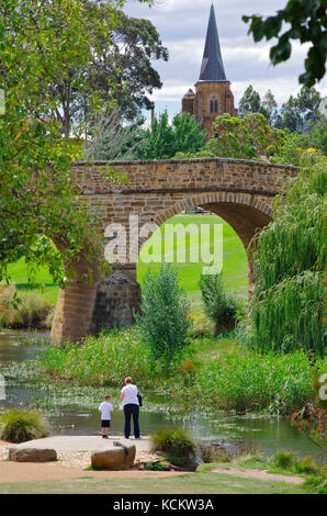 Ein Erwachsener und ein Kind am Coal River, der unter der Richmond Bridge vorbeifließt, mit der St. John’s Catholic Church (1837) im Hintergrund. Richmond, Tasmanien, A Stockfoto