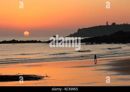 Sonnenaufgang über Coles Beach mit dem Mersey Bluff Lighthouse im Hintergrund und einmunter Spaziergänger. Devonport, Tasmanien, Australien Stockfoto