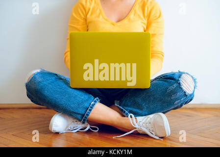 Junge hübsche Frau auf dem Boden sitzend mit Laptop Stockfoto