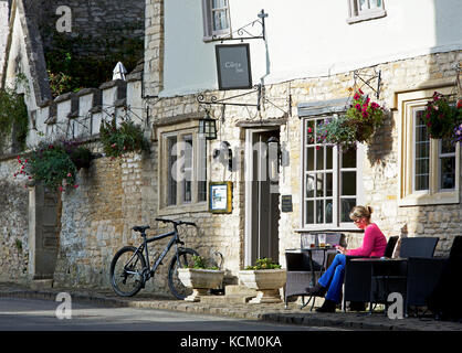 Frau sitzt außerhalb Pub, das Castle Inn, Castle Combe, Wiltshire, England Großbritannien Stockfoto