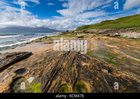 Sandsteinfelsen am Strand in der Bucht von Laig auf der Isle of Eigg, Schottland, Großbritannien. Auf der linken Seite befindet sich die Isle of Rum. Stockfoto