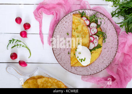 Nützliche französisches Frühstück: rettich Salat und Rucola, pochierte Eier auf einer dünnen crape auf einer Keramikplatte auf weißem Holz- Hintergrund. Ansicht von oben. Stockfoto