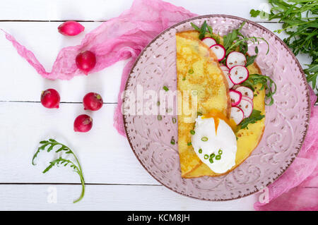 Nützliche französisches Frühstück: rettich Salat und Rucola, pochierte Eier auf einer dünnen crape auf einer Keramikplatte auf weißem Holz- Hintergrund. Ansicht von oben. Stockfoto