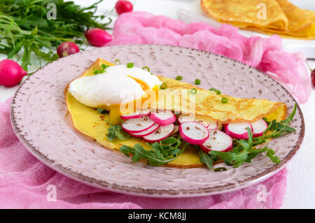 Nützliche französisches Frühstück: rettich Salat und Rucola, pochierte Eier auf einer dünnen crape auf einer Keramikplatte auf weißem Holz- Hintergrund. Stockfoto