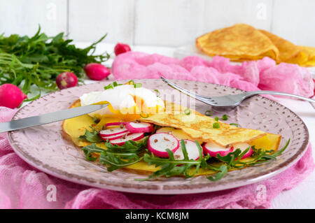 Nützliche französisches Frühstück: rettich Salat und Rucola, pochierte Eier auf einer dünnen crape auf einer Keramikplatte auf weißem Holz- Hintergrund. Stockfoto