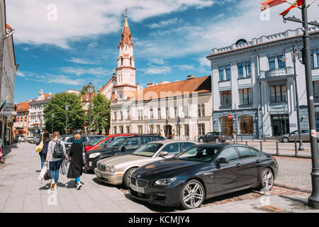 Vilnius, Litauen - 5. Juli 2016: Junge Frauen Menschen zu Fuß in rotuses Straße in der Altstadt. geparkt Luxus autos und St. Nikolaus Kirche im sonnigen Summe Stockfoto