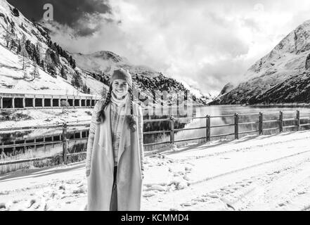 Winter auf höherer Ebene Spaß. Portrait von lächelnden Elegante reisenden Frau gegen Berglandschaft mit See in Alto Adige, Italien Stockfoto