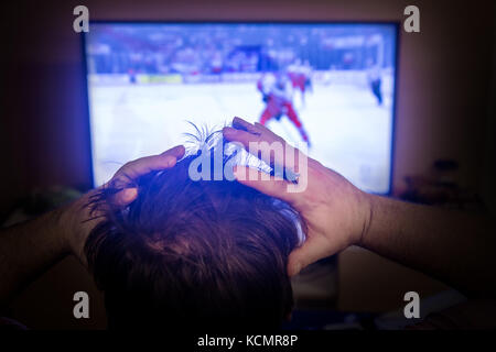 Rückansicht der Aufregung Mann mit Gestik, die Hände wie beobachten Eishockey im Fernsehen zu Hause. Rückansicht der männlichen Kopf beobachten Sport im TV. Stockfoto