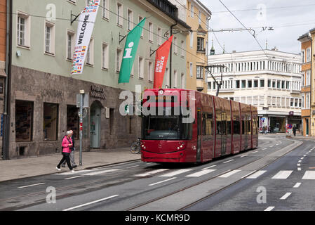 Eine rote elektrische Straßenbahn wurde gestoppt, während ein Paar über die Straße über den Zebrastreifen, Innsbruck, Österreich. Stockfoto