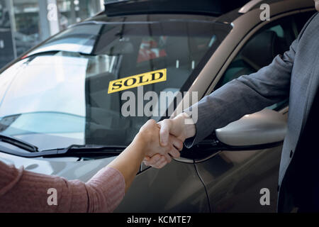 Zugeschnittenes Bild der Verkäufer tun Handshake mit Kunden im Stehen mit dem Auto im Showroom Stockfoto
