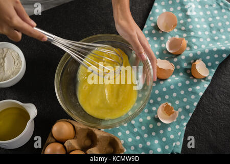 Über dem Kopf der Frau schlagen, Eier mit einem Schneebesen in einer Schüssel Stockfoto
