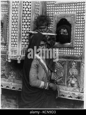 Kind, das auf einem Auge blind ist, an der Schulter der Frau sitzt und saugen Zuckerrohr; und Leiter einer anderen Frau Blick durch Fenster, Ägypten LCCN 2001705646 Stockfoto