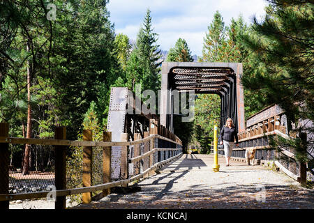 Eine Frau und ihr Golden Retriever (Canis Lupus Familiaris) zu Fuß über einen Bock (Teil der Kettle Valley Railway) in Kettle River Provincial Park in der Nähe von Rock Creek, British Columbia. Stockfoto