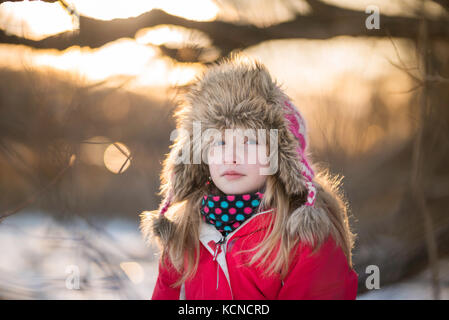 Mädchen (10) sitzen auf dem Baum am Ufer eines zugefrorenen See im Winter. Stockfoto