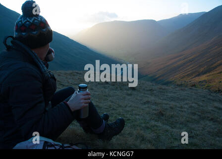 Wanderer in wolliger Hut trinken von Thermos Blick über Wasdale von Abstieg von Great Gable über Styhead Tarn, Yewbarrow im Hintergrund, Lake Distric Stockfoto