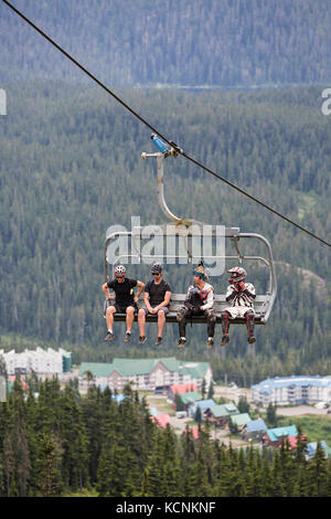 Mountainbiker fahren mit dem Hawk Sessellift mit dem Dorf am Mt. Washington im Hintergrund. Mt. Washington, Comox Valley, Vancouver Island, British Columbia, Kanada. Stockfoto