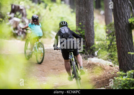 Weibliche Mountainbiker fahren hinunter zum Mt. Washington Dorf entlang der Green Mile Radweg in Mt. Washington, Comox Valley, Vancouver Island, British Columbia, Kanada Stockfoto