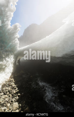 Ein Wanderer schaut auf eine Schneehöhle am Fuße des Century Sam Sees. Strathcona Park, Vancouver Island, British Columbia, Kanada Stockfoto