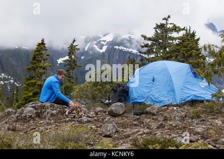 Ein junger Wanderer neigt zum Feuer während des Campens auf Lee Plateau, Vancouver Island, British Columbia, Kanada. Stockfoto