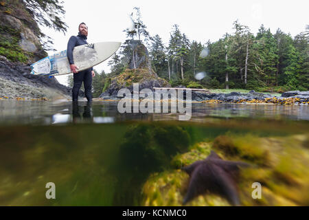 Ein Surfer in seiner wässrigen Element sieht die Brandung Pause inmitten einer niedrigen Gezeiten Pool, Spring Island in der Nähe von Kyuquot, Vancouver Island, British Columbia, Kanada Stockfoto