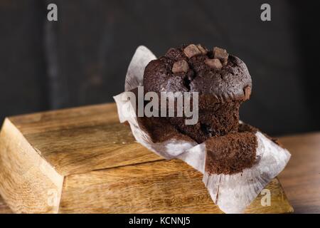 Teilweise ausgewickelt Schokolade chunks Muffin auf dunklen Holz und schwarzer Hintergrund Stockfoto