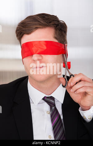 Geschäftsmann schnitt seine Augenbinde mit Sprungfeder in Office Stockfoto