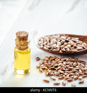Brauner Leinsamen in Löffel und Leinsamenöl in Glasflasche auf weißem Holz- Hintergrund. Leinöl ist reich an Omega-3-Fettsäuren. Kopieren Sie Platz. Platz Stockfoto