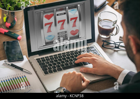 Online gambling Konzept. Mann mit einem Laptop, Slot Machine auf dem Bildschirm, Büro Hintergrund Stockfoto