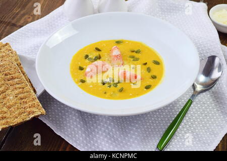 Kürbispüree Suppe mit Garnelen in eine weiße Platte auf einem hölzernen Hintergrund. gesunde Ernährung Konzept Stockfoto