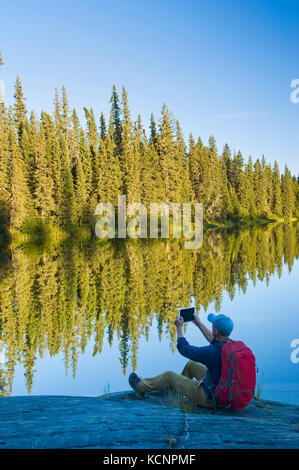 Ein Wanderer nimmt ein Foto mit einem Tablet, entlang der Grass River, Northern Manitoba, Kanada Stockfoto