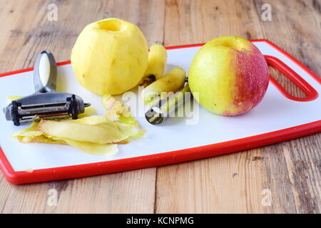 Geschälte Äpfel mit dem Kern entfernt mit speziellen Messern auf einem weißen Schneidbrett auf einer hölzernen Hintergrund genommen. Schritt für Schritt gesund Essen kochen. Stockfoto