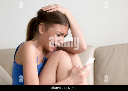 Schluchzend jugendlich Mädchen Messaging auf Telefon, Weinen gedrückt junge Dame hält Telefon sitzen auf einem Sofa, frustrierte Frau in Tränen auf Zelle Gefühl rejec Stockfoto