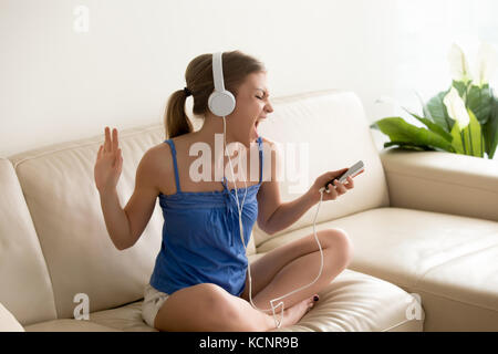 Musik fan Liebhaber mit Kopfhörern hören bevorzugten Audio Track zu Hause auf der Couch smartphone Holding, jugendlich Mädchen singen Neue beliebte Lied enjoyi Stockfoto