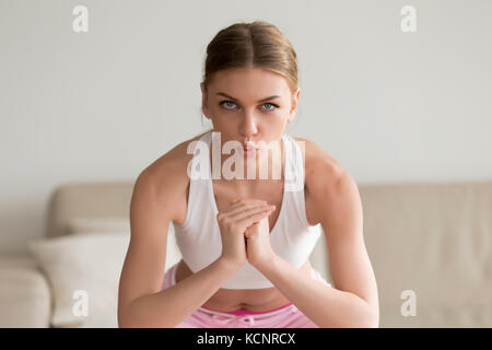 Junge sportliche schlanke Frau tun Hocke Morgen üben, üben die Atmung richtig während Arbeiten home Routine, Kamera, Hände halten Stockfoto