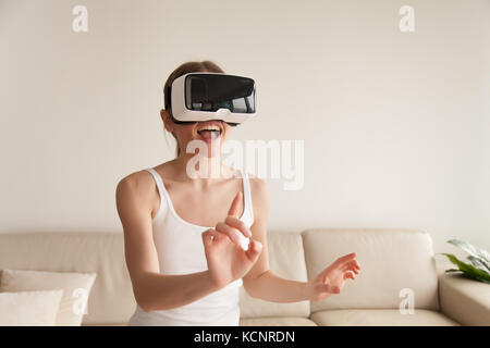 Interessierte begeisterte Frau, die eine Schutzbrille trägt, die die virtuelle Welt mit dem Finger berührt, neugierige glückliche junge Frau im VR-Headset genießt AR Tour und macht Einkäufe in Stockfoto