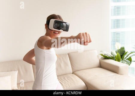 Junge Teenager-Gamer mit Augmented-Reality-Brille, die in Boxhaltung steht und Action-Simulatorspiel-App spielt, weibliche Spielerin kämpft mit FIS Stockfoto