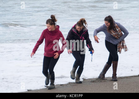 Aberystwyth Wales UK, Samstag 07 Oktober 2017 UK Wetter: drei junge Frauen werden von den Wellen gefangen, während sie an einem bewölkten und luftigen Herbstnachmittag am Strand entlang laufen. Foto: keith morris/Alamy Live News Stockfoto