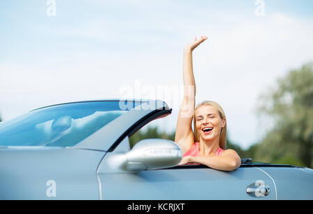 Glückliche junge Frau in Cabrio Hand winken Stockfoto