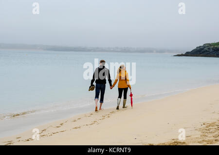 Kupplung auf Porthminster Beach halten sich an den Händen. Mann barfuß, während Frau weras Gummistiefel und trägt Regenschirm. Stockfoto