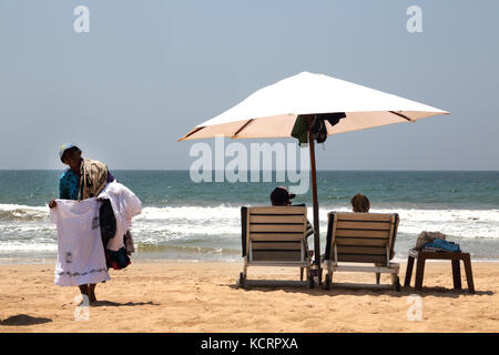 Bentota Sri Lanka Paar am Strand unter einem Sonnenschirm und hawker Verkauf tops Stockfoto