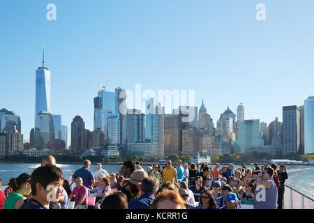 Menschen und Touristen fotografieren und mit Blick auf die Skyline von New York von der Fähre an einem sonnigen Tag Stockfoto