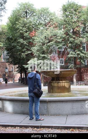 Ein Mann steht in der Nähe eines Springbrunnens im historischen Boston mit einer Kameratasche, um die Sehenswürdigkeiten zu sehen Stockfoto