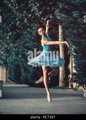 Tanzende Ballerina in blauer tutu Ballett und auf europäischen Straße mit Bäumen im Sommer oder Herbst. Junge schöne Brünette Frau üben stretchin Stockfoto